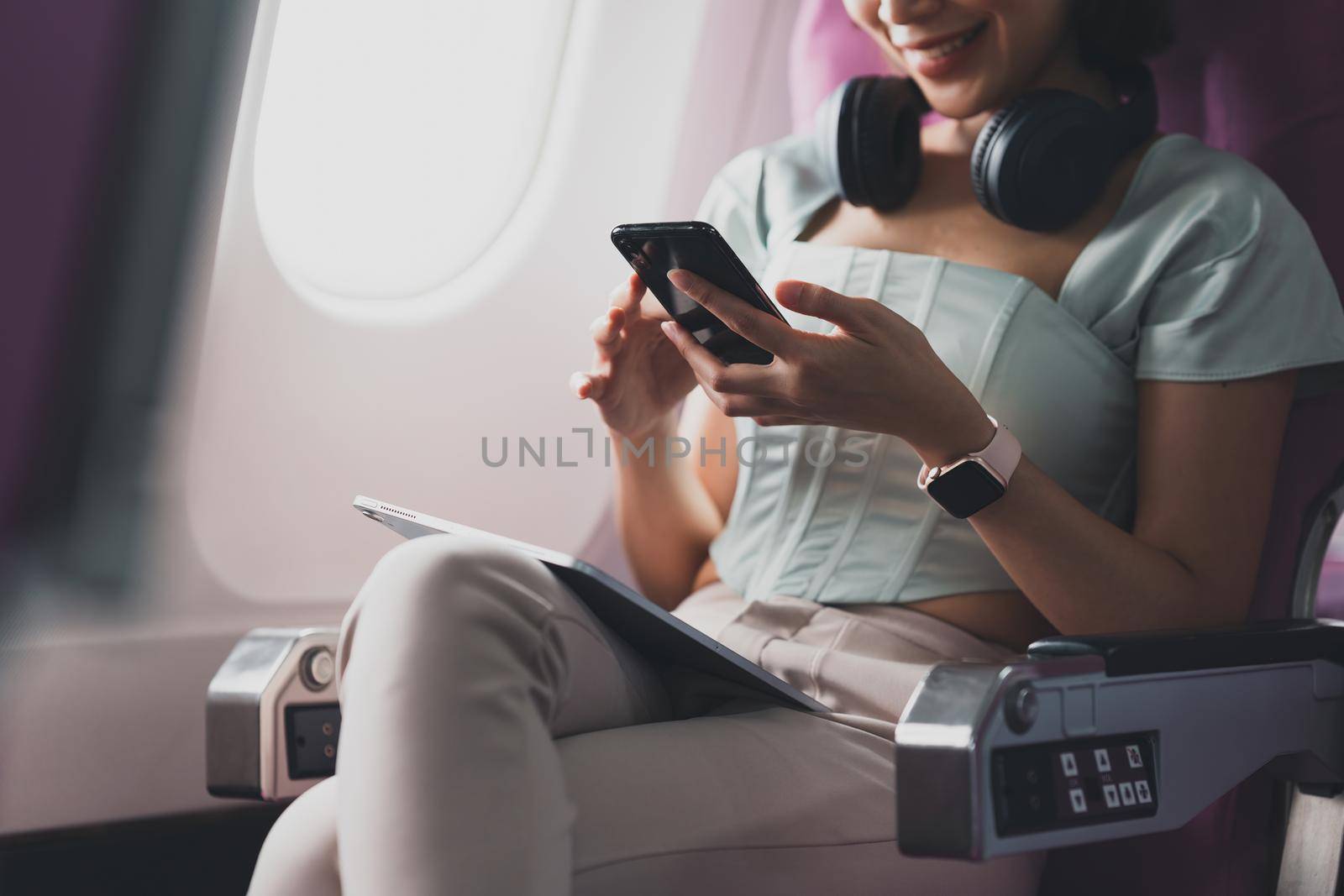 Young asian woman using smartphone connected to wifi internet during flight on board. Travel concept.