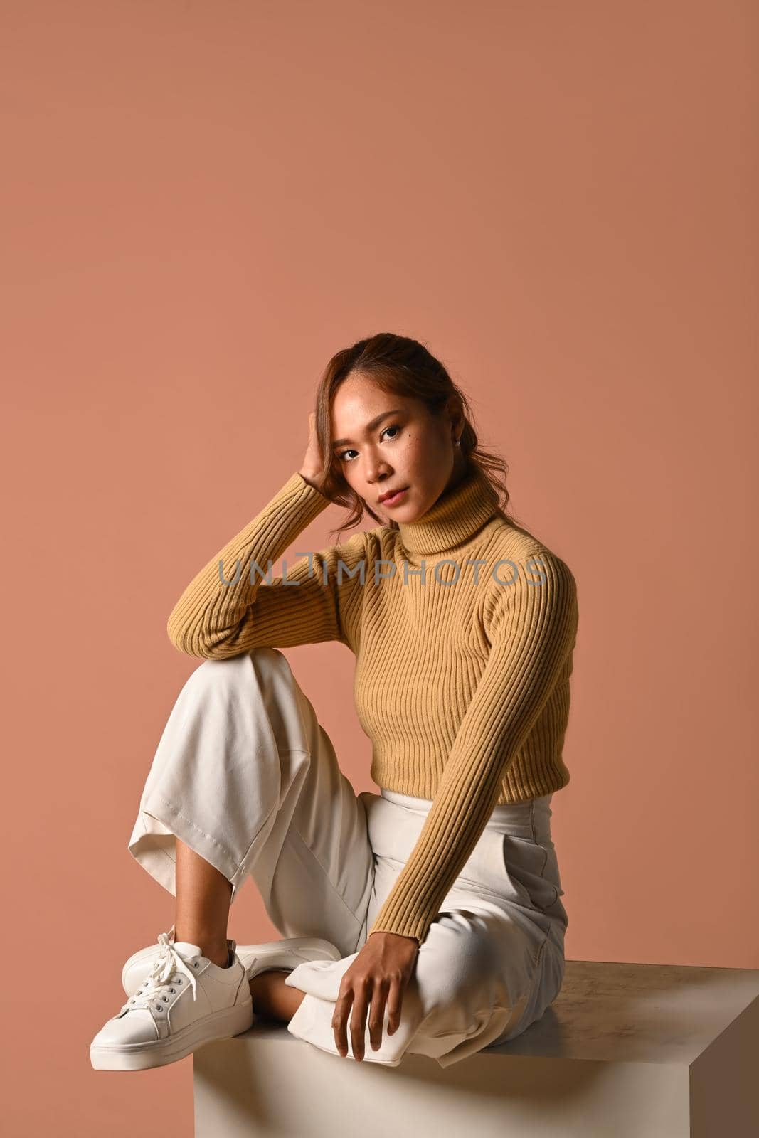 Portrait of trendy woman wearing warm sweater sitting on pink background. Fashion studio photo, Autumn and Winter concept.