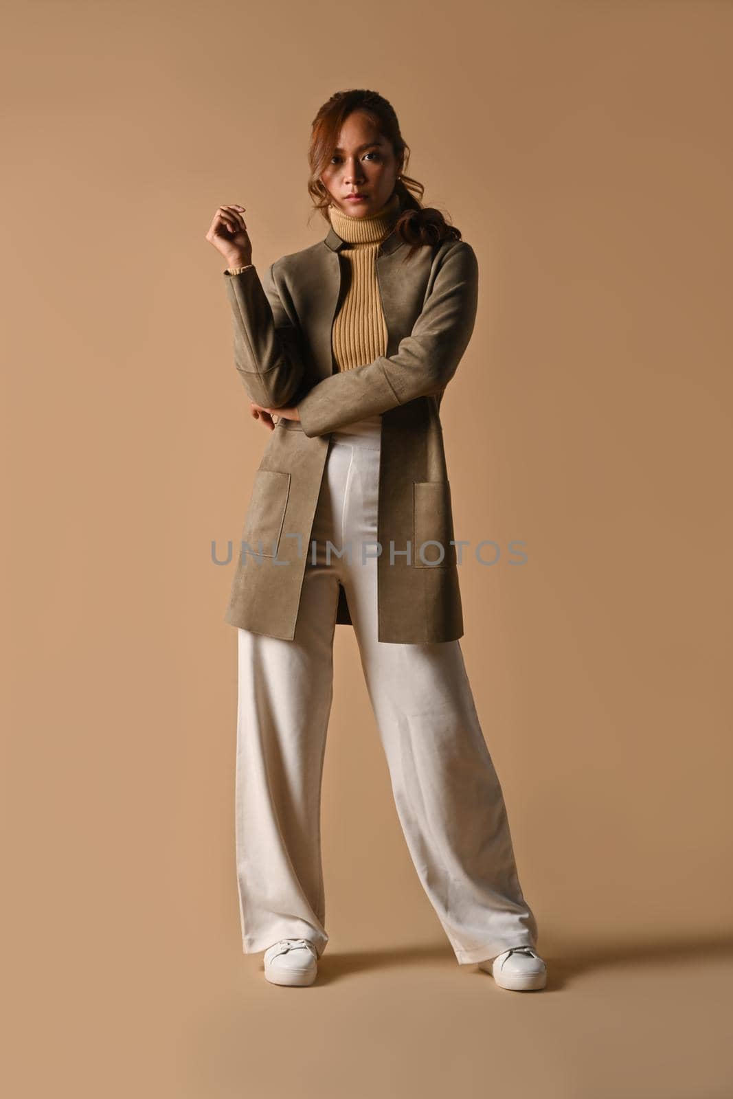 Full length portrait of beautiful young woman stylish autumn outfits standing on beige background.