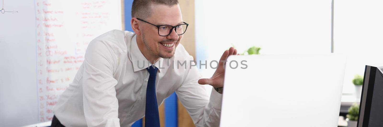 Portrait of smiling worker wave hi to online colleagues on video call. Computer on desk, board with lettering on wall. Business, conference meeting concept