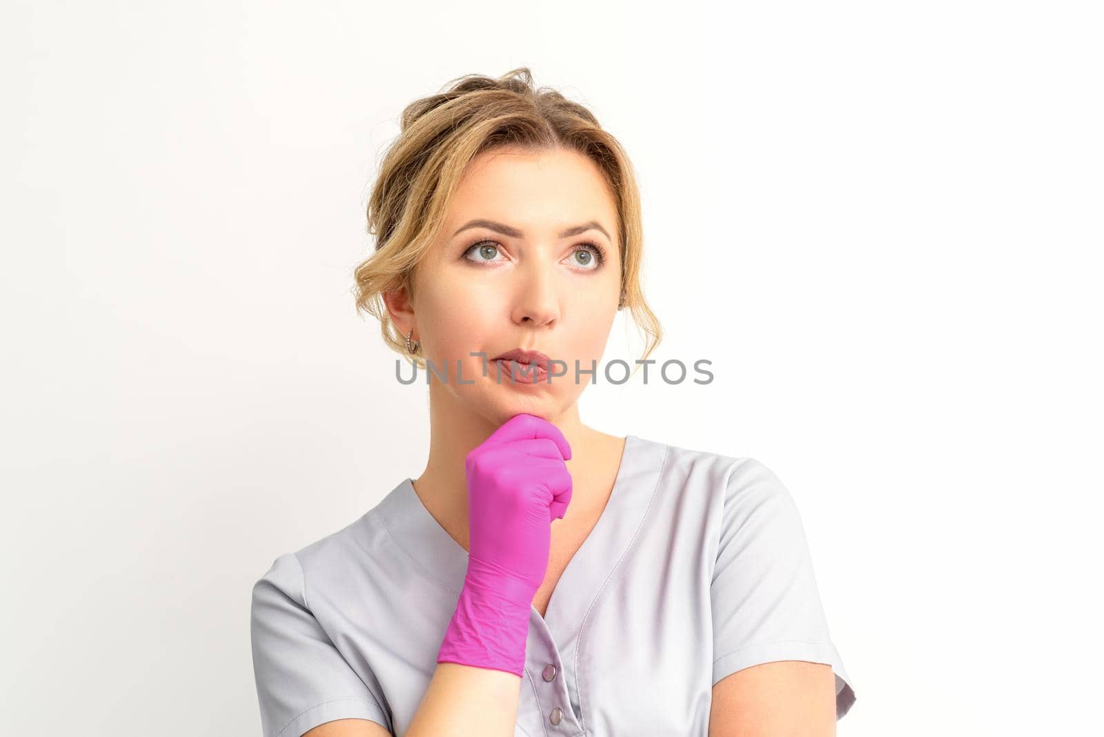 Young caucasian female doctor wearing gloves thoughtful looking away against a white background. by okskukuruza