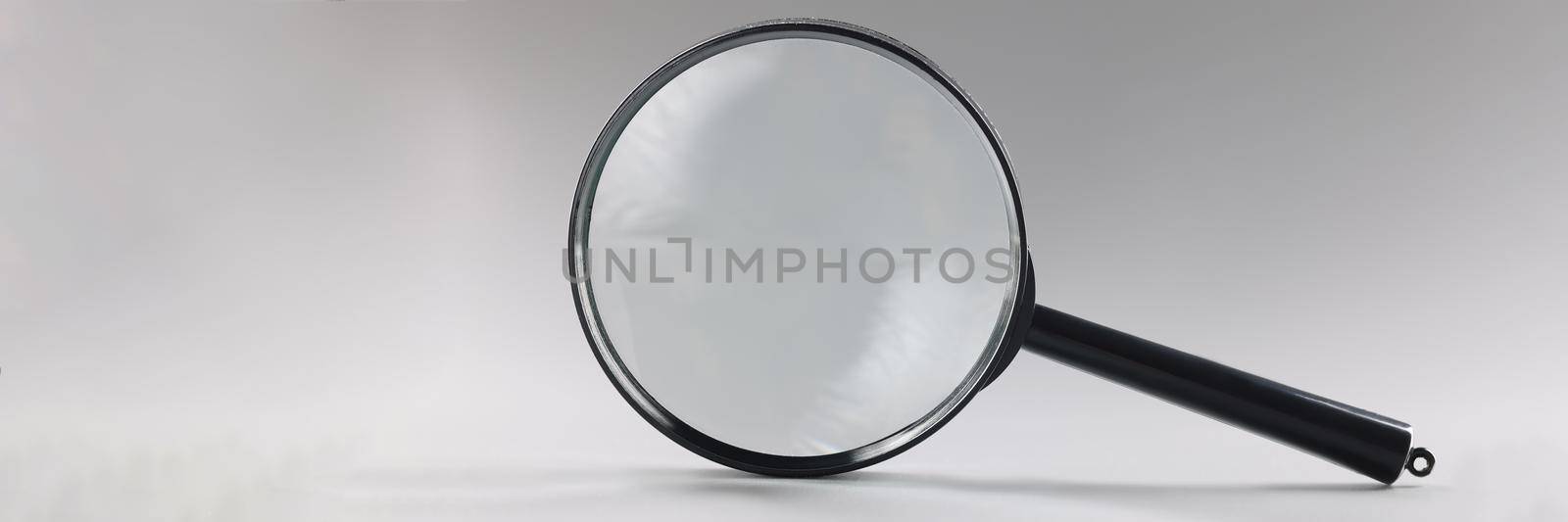 Close-up of single magnifying glass with black handle, leaning on grey surface. Simple design of lens or loupe to enlarge objects. Magnifying lens concept