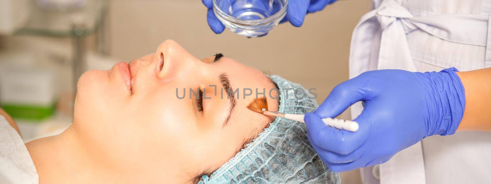 Young white woman getting acid organic retinol peel face skin with the brush in a beauty clinic