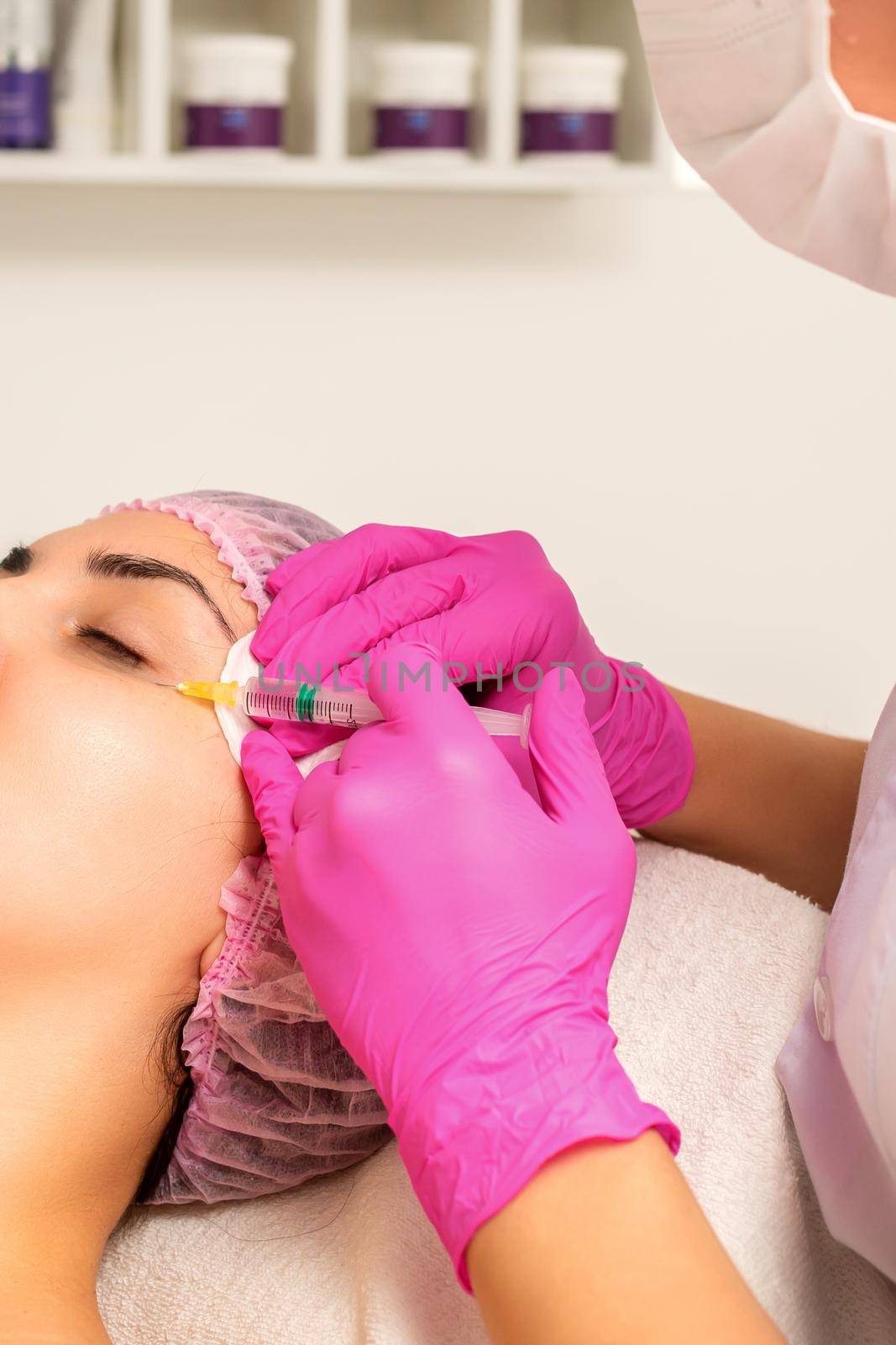 The young white woman is getting rejuvenating facial injections with hyaluronic acid on the eye in a beauty clinic