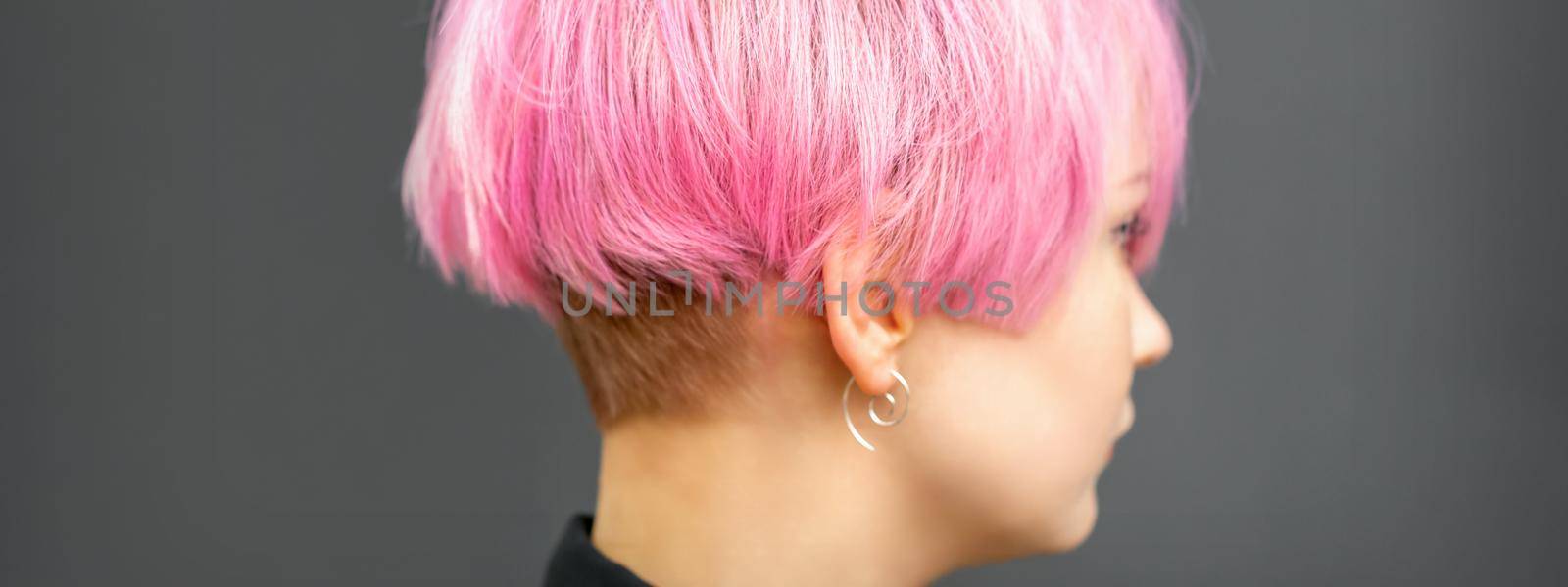 Profile of a beautiful young caucasian woman with short bob pink hairstyle on dark gray background