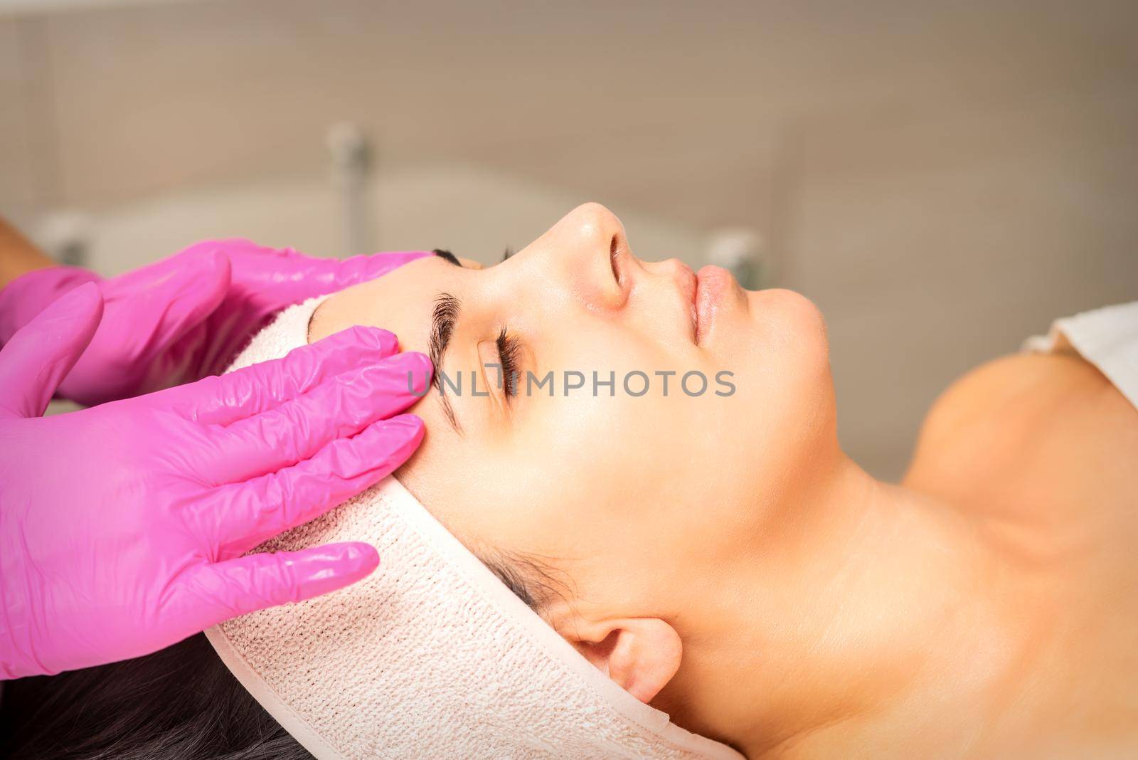 Cosmetologist with gloved hands applies a moisturizing mask with peeling cream on the female face. Facial cosmetology treatment. Procedures for facial care. by okskukuruza