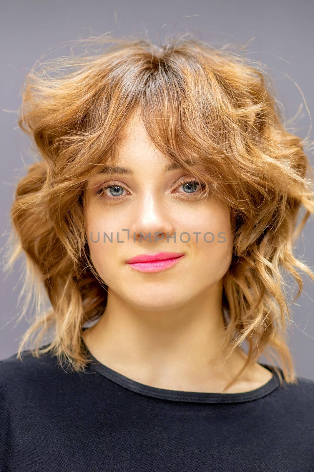 Portrait of a beautiful young caucasian red-haired woman with short wavy hairstyle smiling and looking at camera on dark gray background with copy space. by okskukuruza