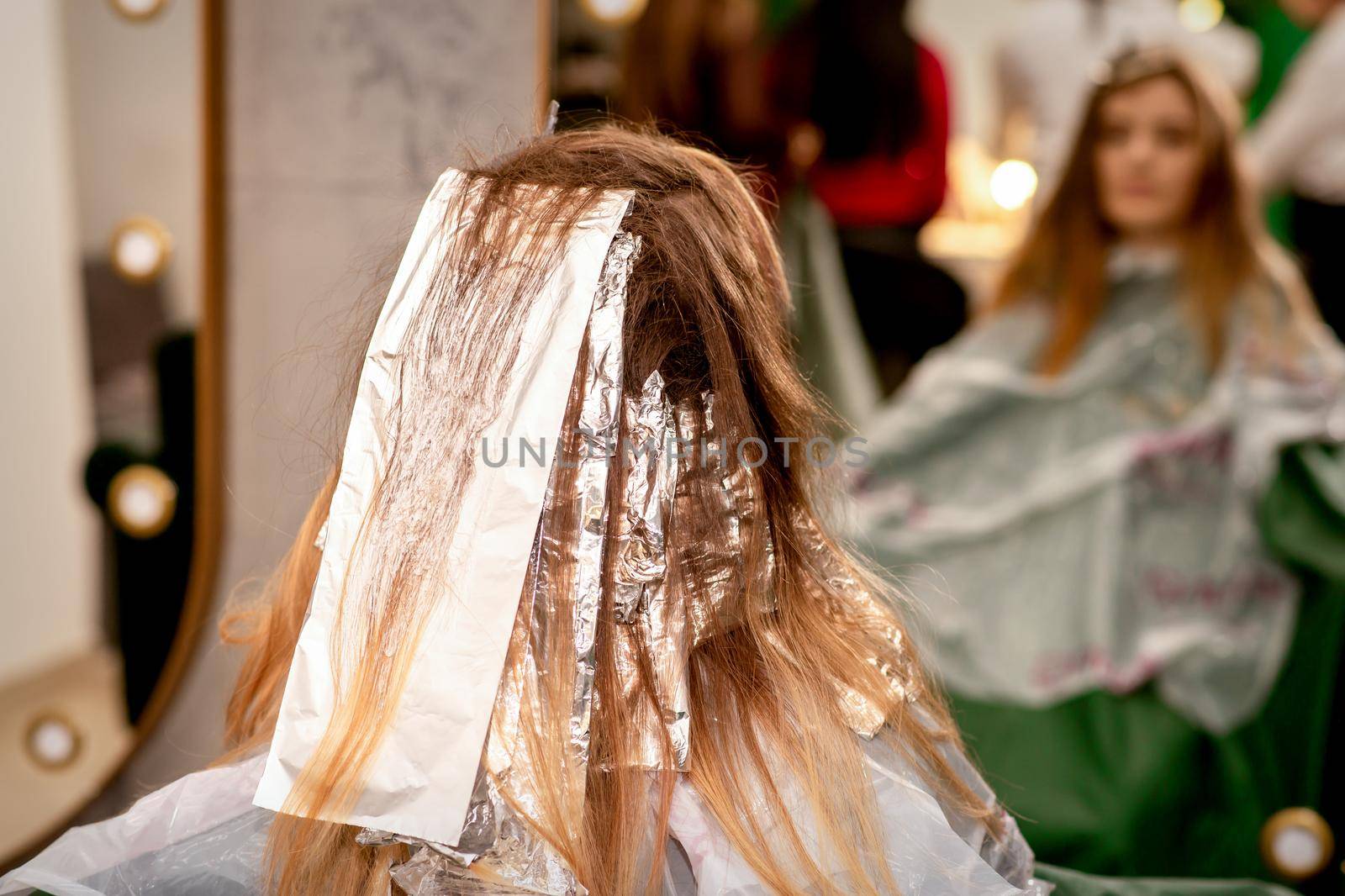 Beautiful young caucasian woman with foil in her hair while dyeing her hair sitting in a beauty salon. by okskukuruza