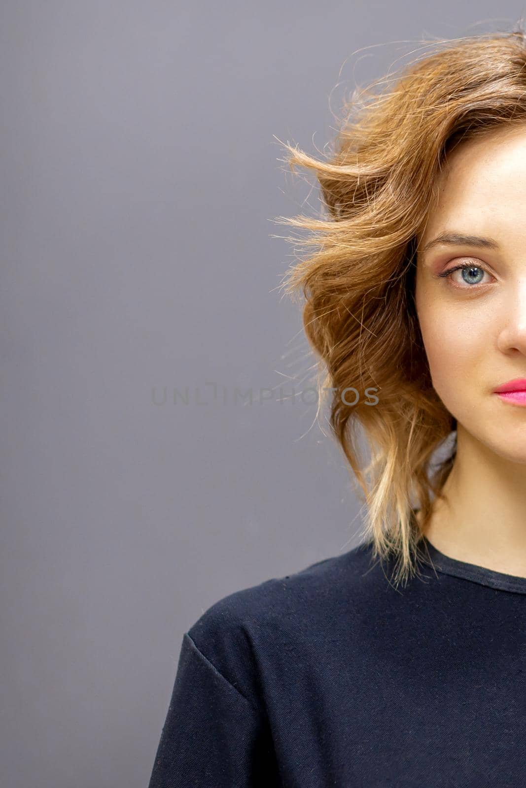 Portrait of a beautiful young caucasian red-haired woman with short wavy hairstyle smiling and looking at camera on dark gray background with copy space