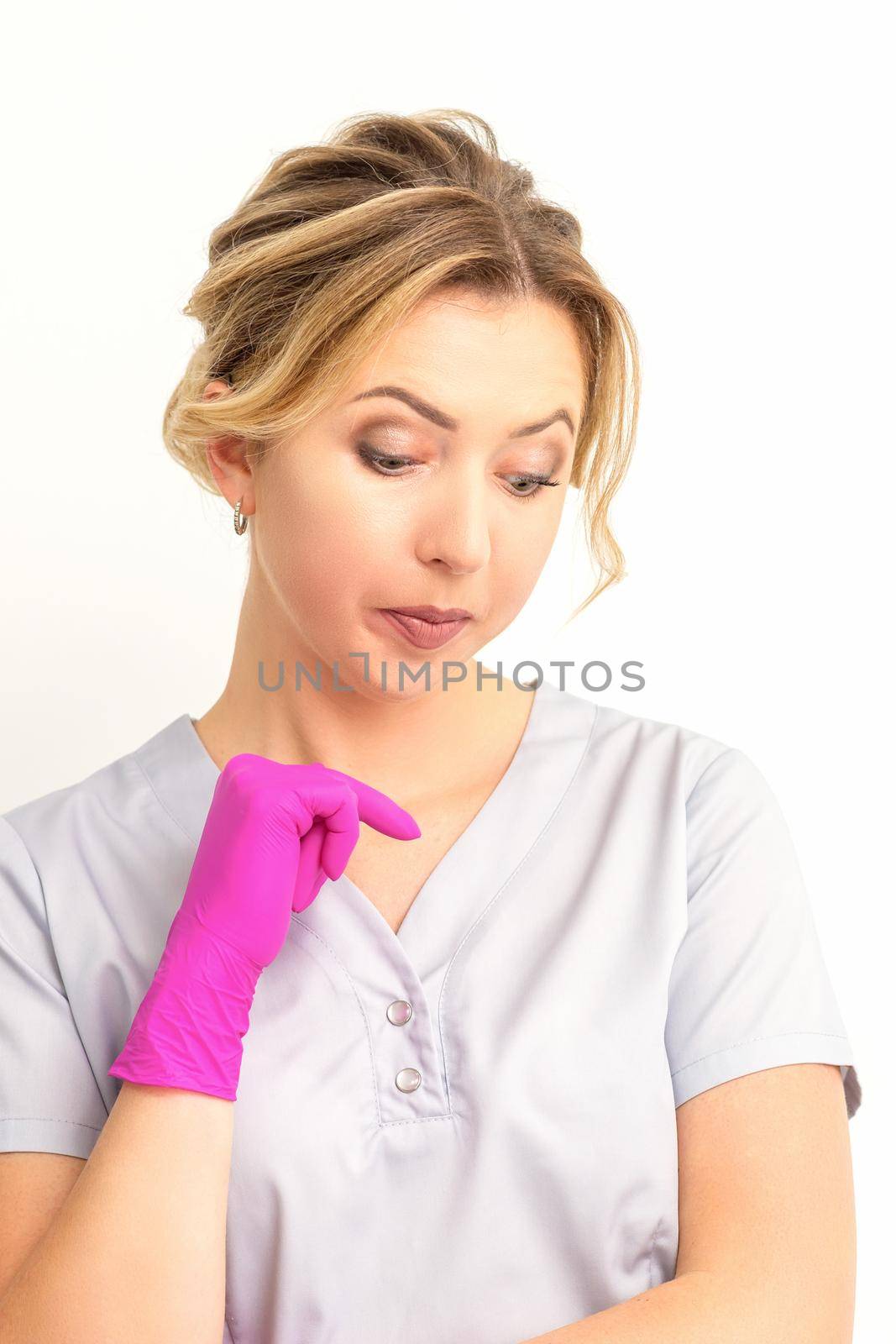 Young caucasian female doctor wearing gloves thoughtful looking down against a white background. by okskukuruza