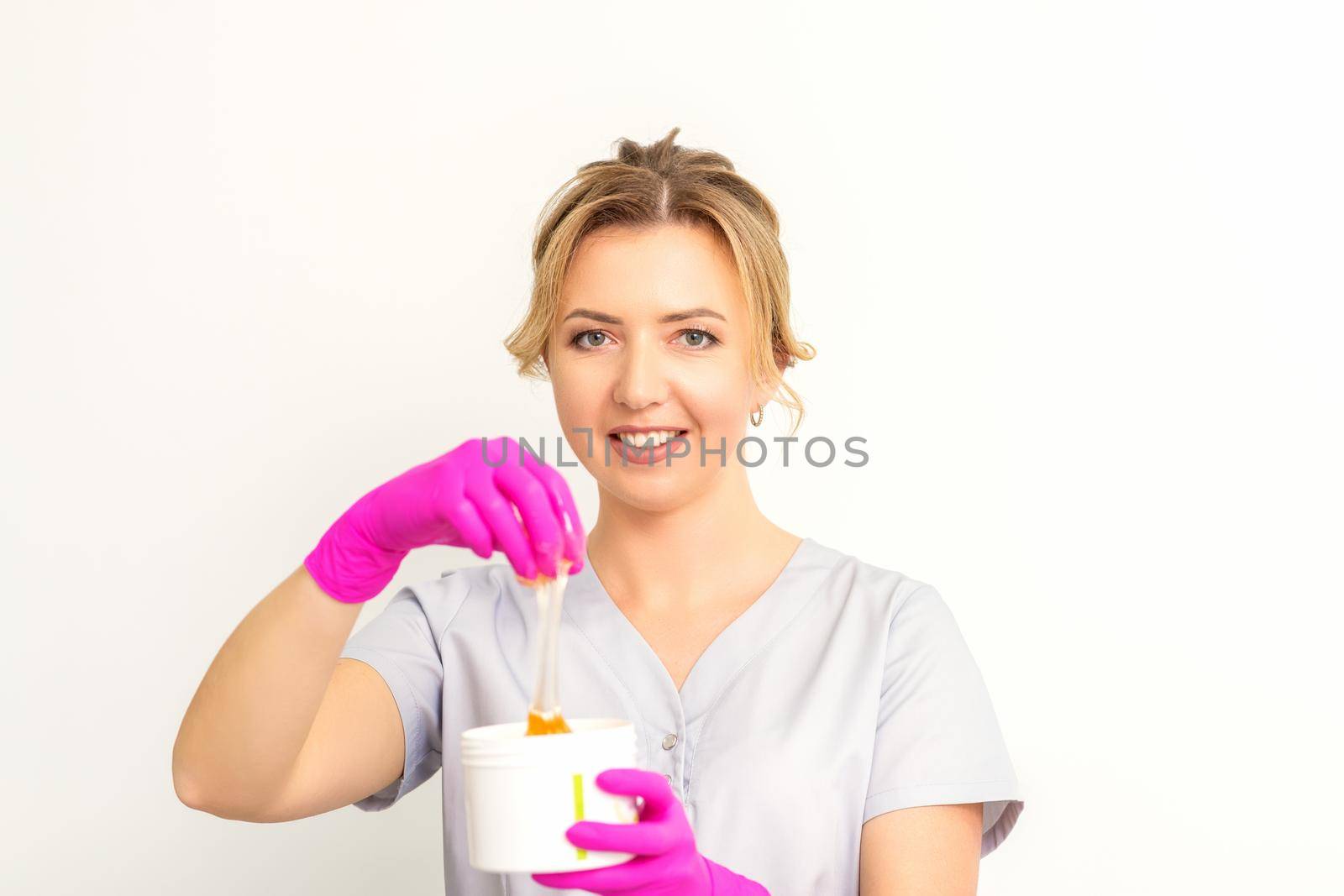 Portrait of a female caucasian beautician holding a jar of sugar paste for sugaring wearing pink gloves on white background. by okskukuruza