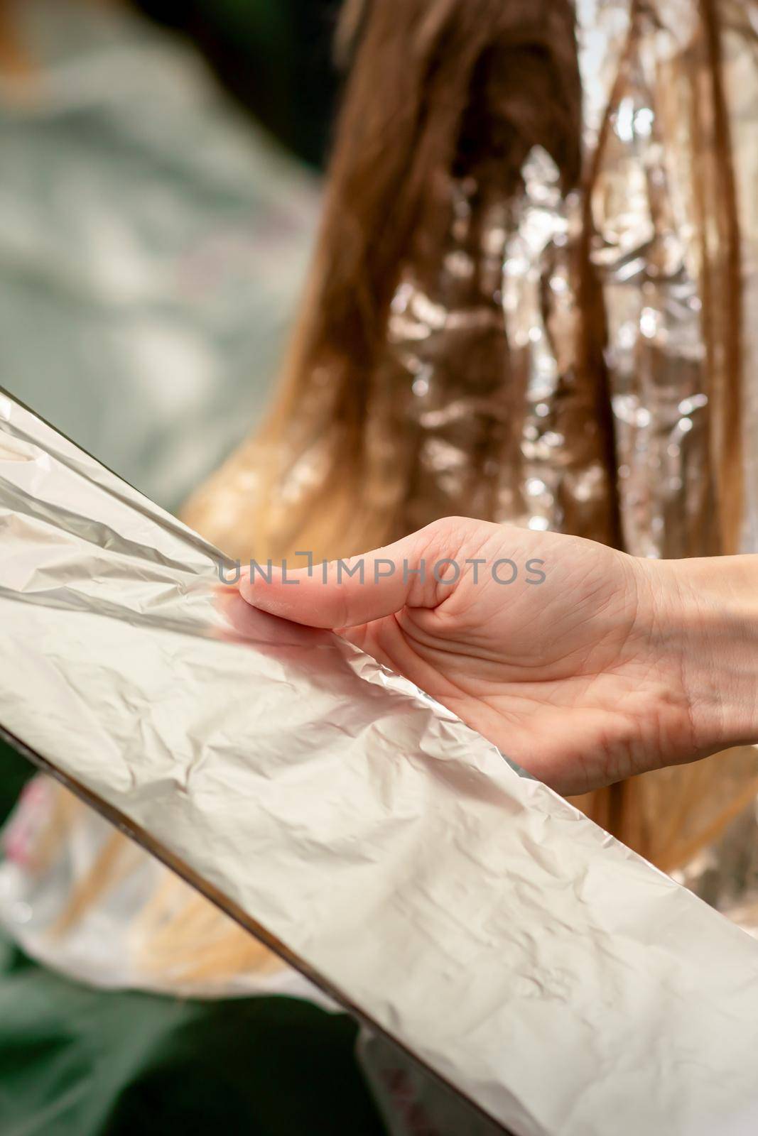 Hairdresser's Hands Holding Foil Sheet For Hair Dye In Beauty Salon. by okskukuruza