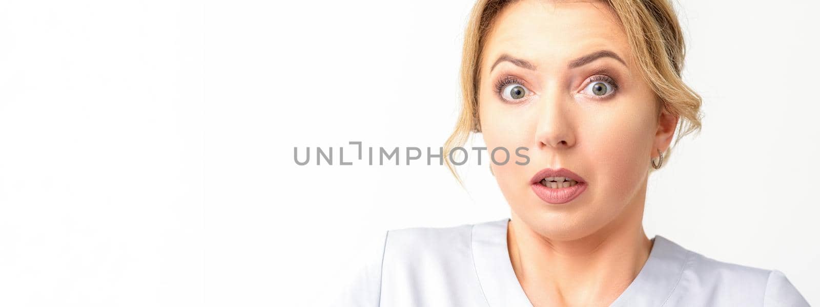 Female doctor shocked. Close up portrait of a young caucasian woman looking surprised with wide eyes stared isolated white wall background. by okskukuruza