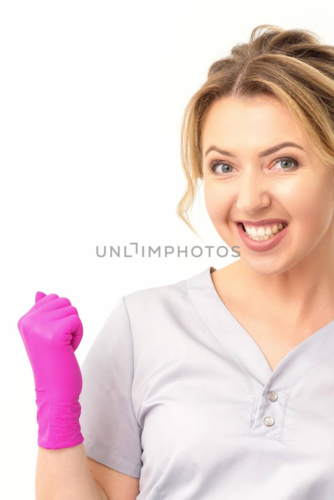 Happy caucasian woman doctor wearing pink gloves celebrates and raising fists on white background. by okskukuruza