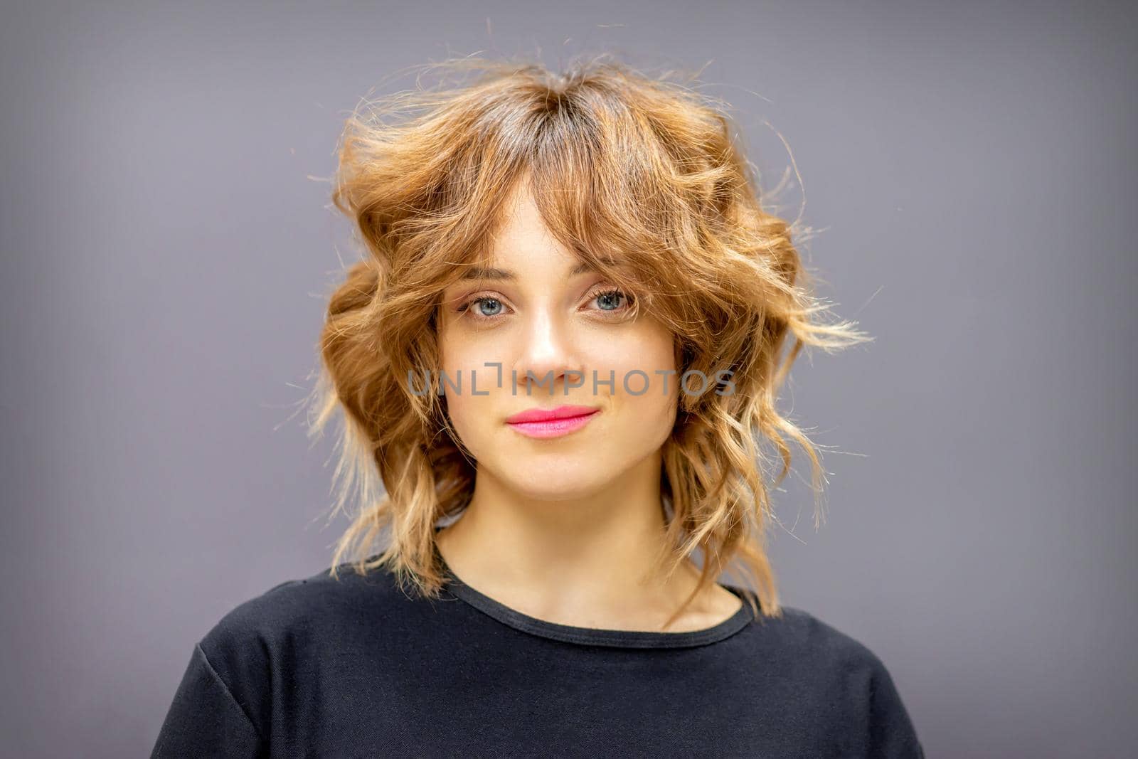 Portrait of a beautiful young caucasian red-haired woman with short wavy hairstyle smiling and looking at camera on dark gray background with copy space