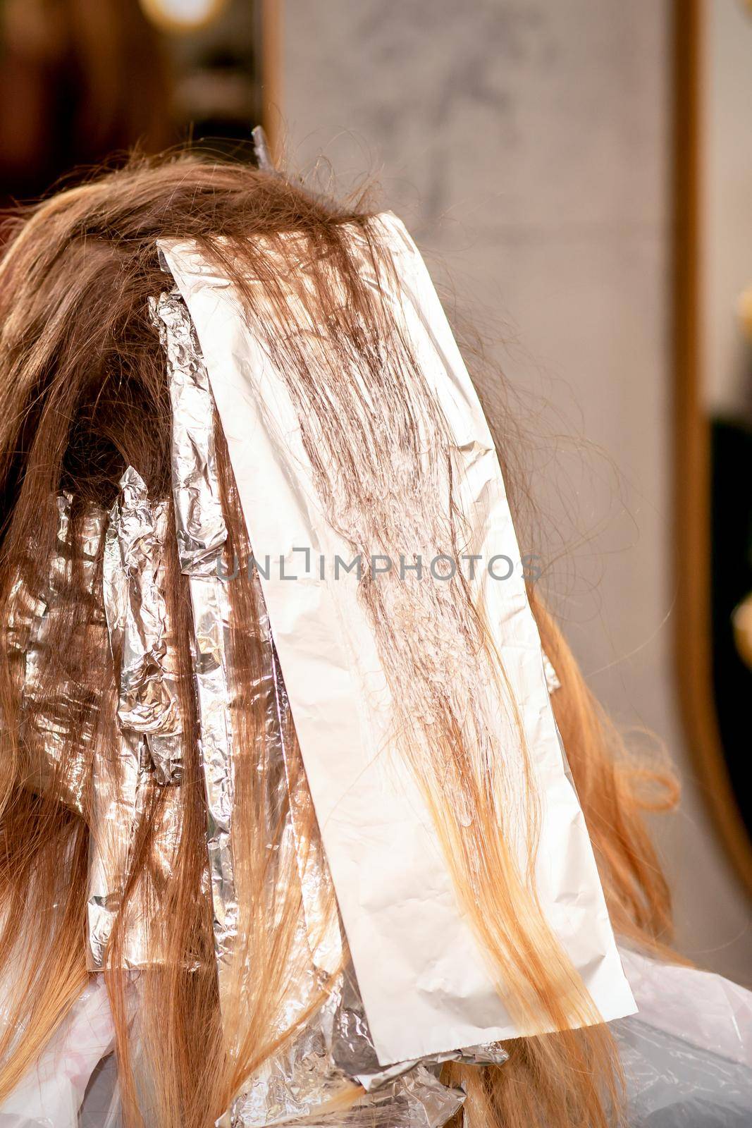Beautiful young caucasian woman with foil in her hair while dyeing her hair sitting in a beauty salon. by okskukuruza