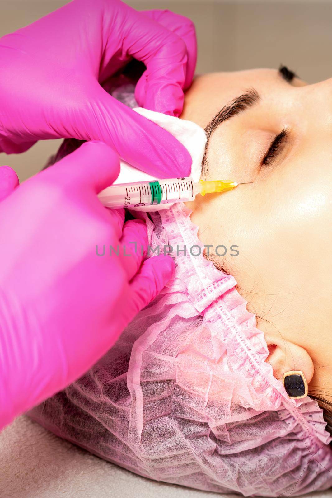 The young white woman is getting rejuvenating facial injections with hyaluronic acid on the eye in a beauty clinic