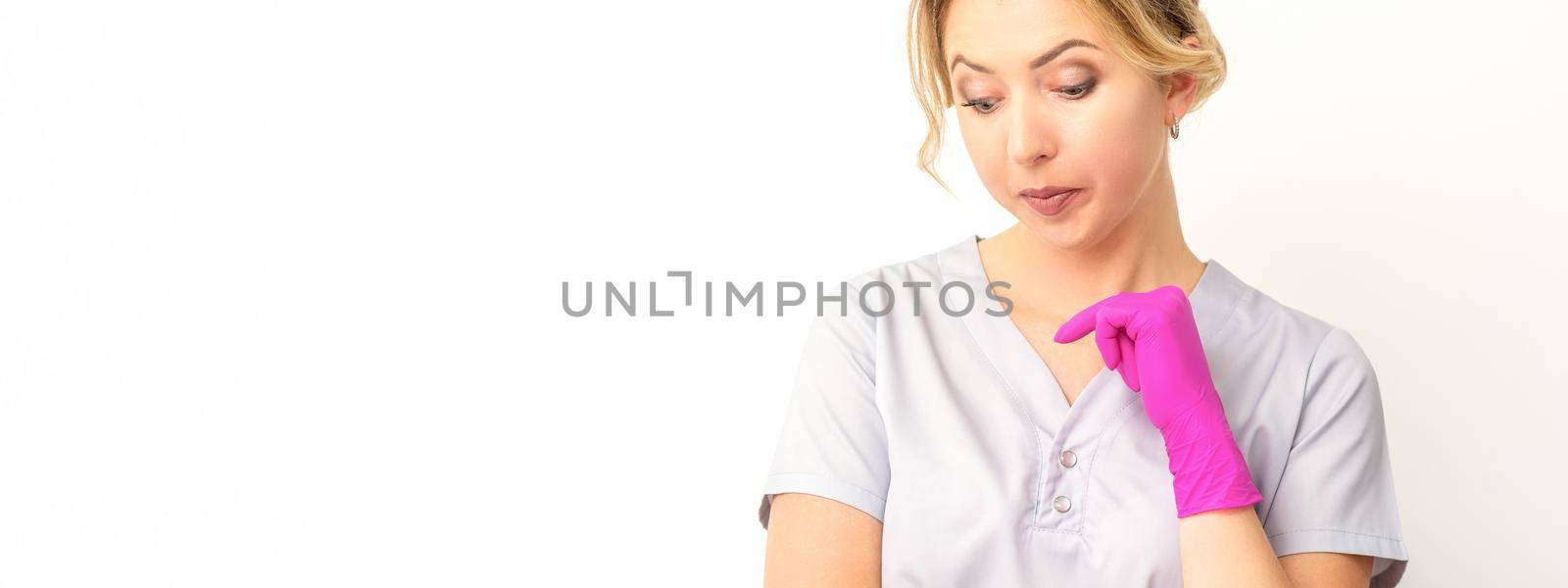 Young caucasian female doctor wearing gloves thoughtful looking down against a white background. by okskukuruza