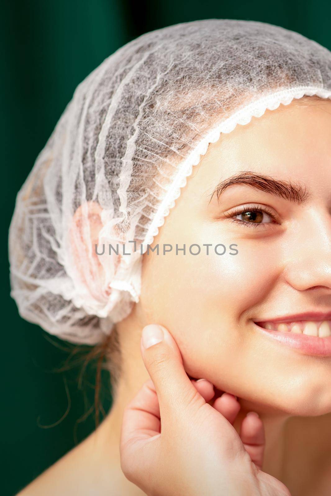 Plastic surgery and beauty concept. Professional cosmetician examining and touching the face of the beautiful young caucasian smiling woman in a clinic of esthetic cosmetology. by okskukuruza