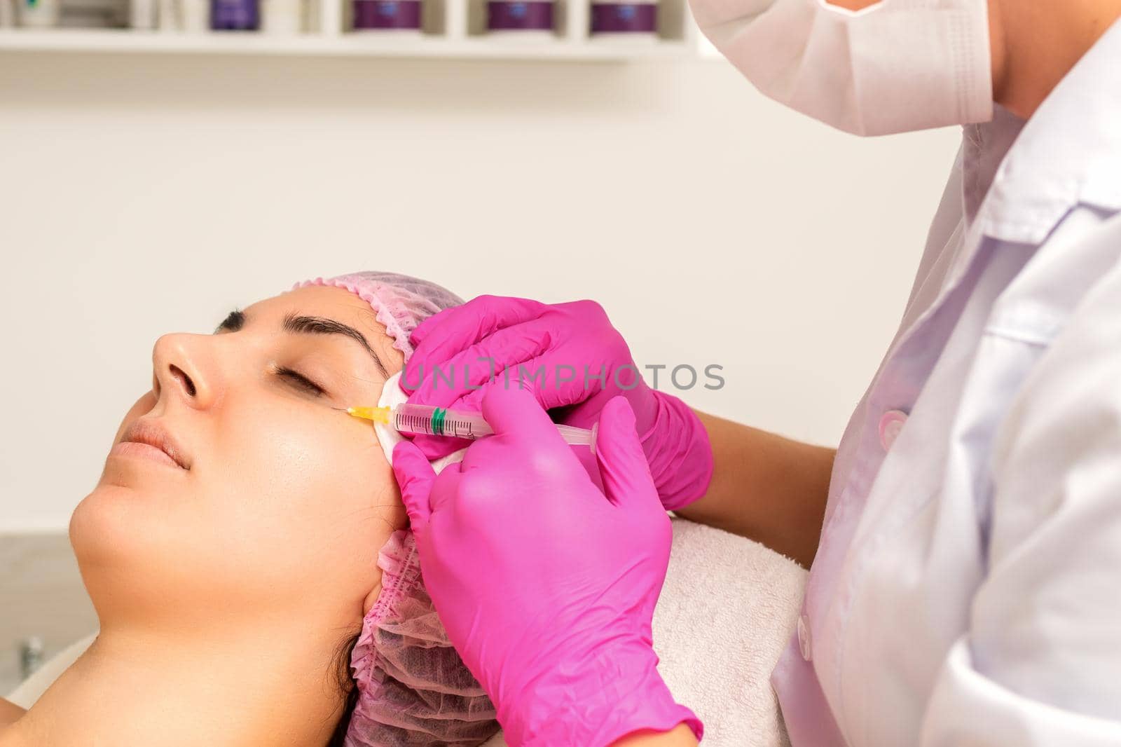 The young white woman is getting rejuvenating facial injections with hyaluronic acid on the eye in a beauty clinic