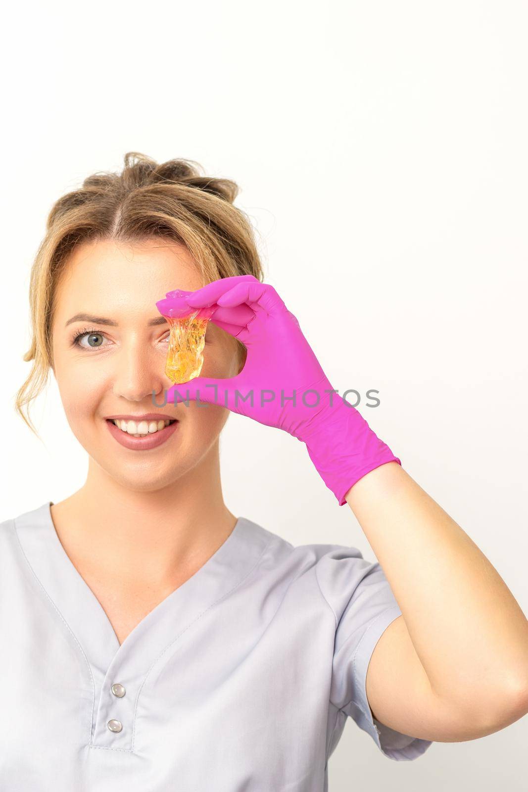 The master of sugar hair removal holds liquid yellow sugar paste, covering her eye with wax for depilation on a white background