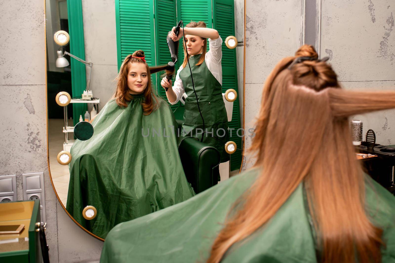The hairdresser is drying long brown hair with a hairdryer and round brush in a beauty salon. by okskukuruza