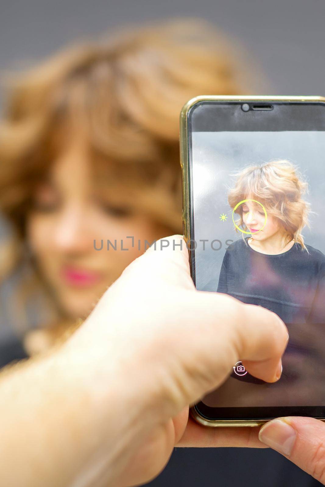 Man hairdresser taking pictures on the smartphone of her client's hairstyle against a gray background. by okskukuruza