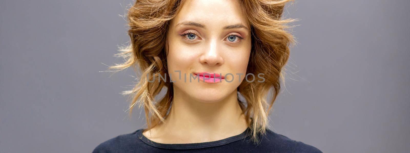 Portrait of a beautiful young caucasian red-haired woman with short wavy hairstyle smiling and looking at camera on dark gray background with copy space