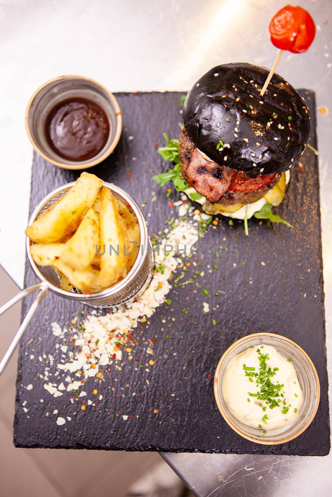Black burger with french fries on stone cutting board.In kitchen restaurant