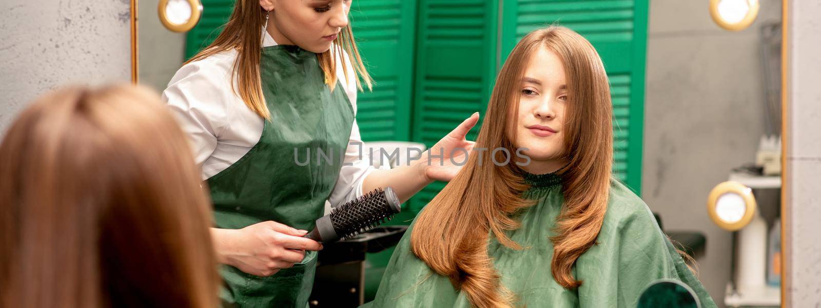 Professional hair care. Young female red-haired with long hair receiving hairstyling in a beauty salon.