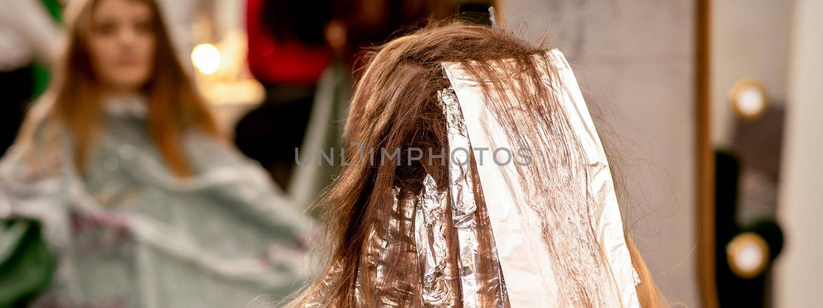 Beautiful young caucasian woman with foil in her hair while dyeing her hair sitting in a beauty salon