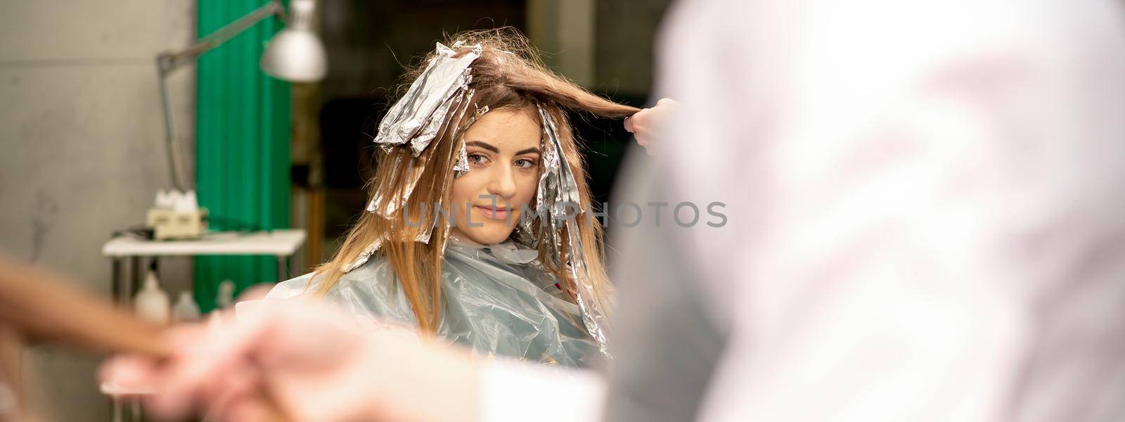 Portrait of a beautiful young caucasian woman who is smiling getting dyeing her hair with foil in a beauty salon