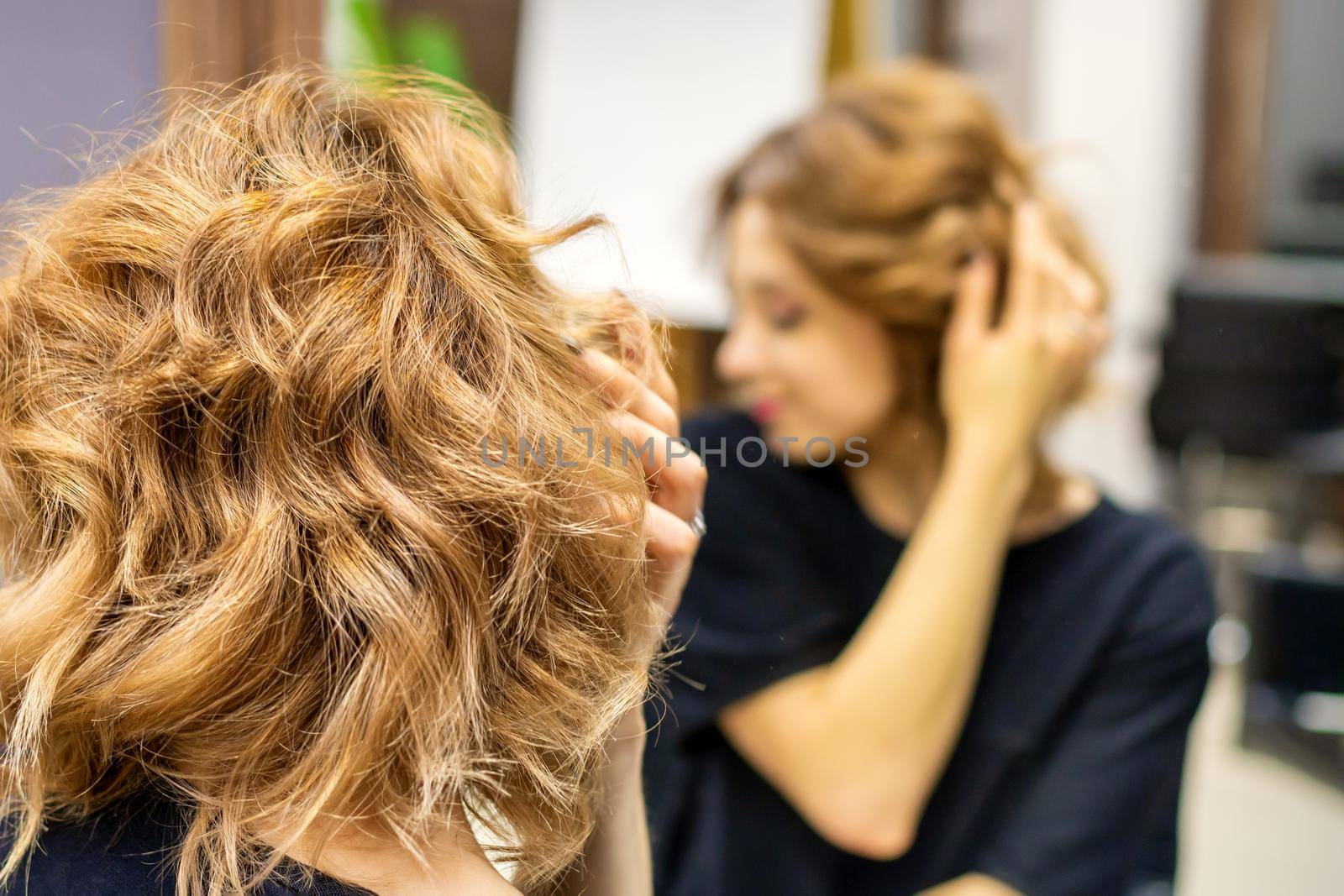 Young woman checking her new curly brown hairstyle in front of the mirror at the hairdresser salon by okskukuruza