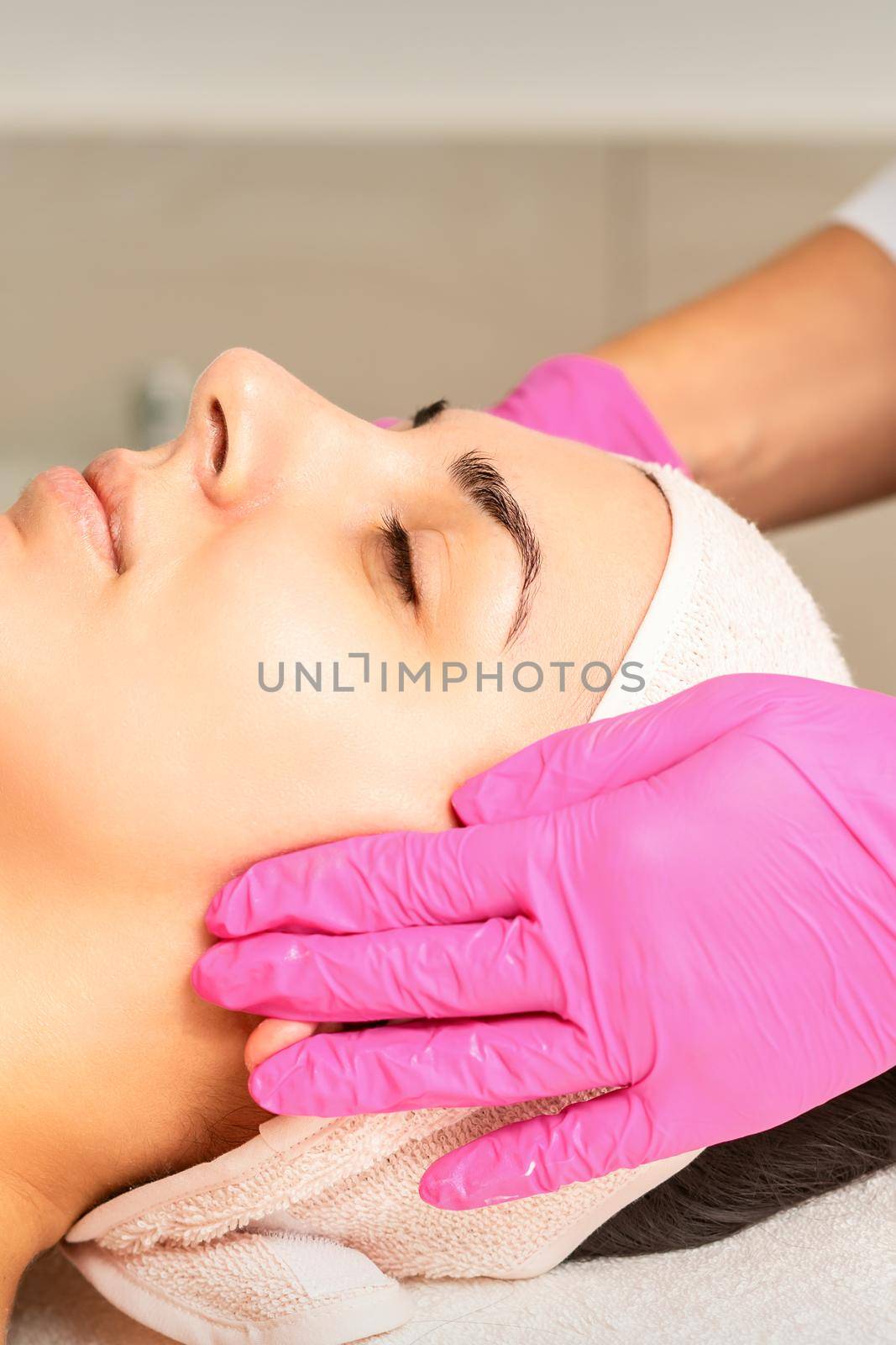 Cosmetologist with gloved hands applies a moisturizing mask with peeling cream on the female face. Facial cosmetology treatment. Procedures for facial care. by okskukuruza