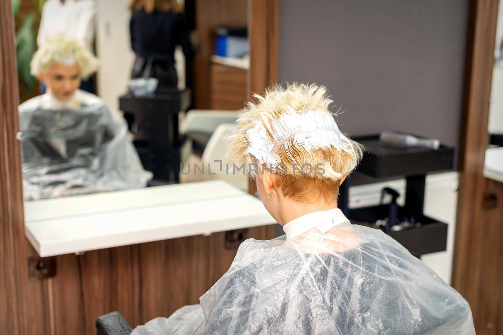 Coloring white hair with hair dye of the young caucasian blonde woman sitting at a hair salon, close up. by okskukuruza