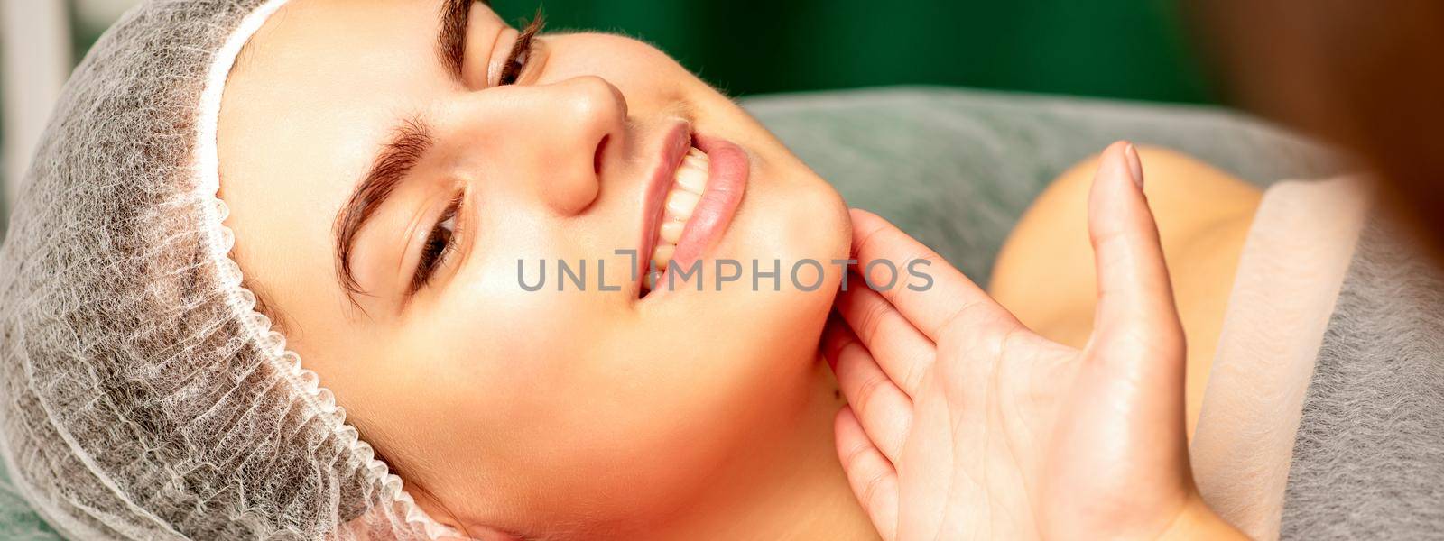 Plastic surgery and beauty concept. Professional cosmetician examining and touching the face of the beautiful young caucasian smiling woman in a clinic of esthetic cosmetology