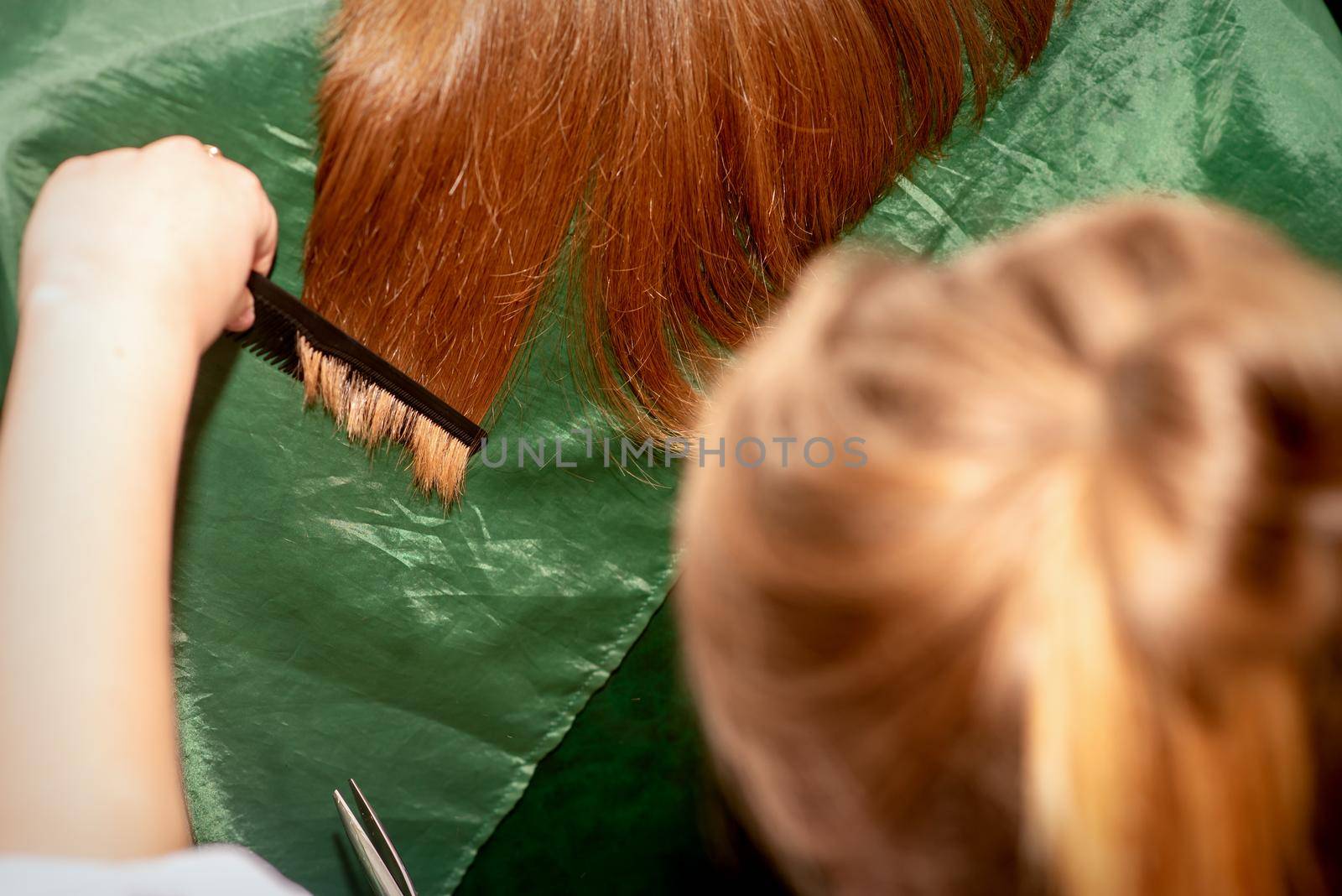 A hairdresser does a haircut and combes the long hair of a brunette woman in a beauty salon. by okskukuruza