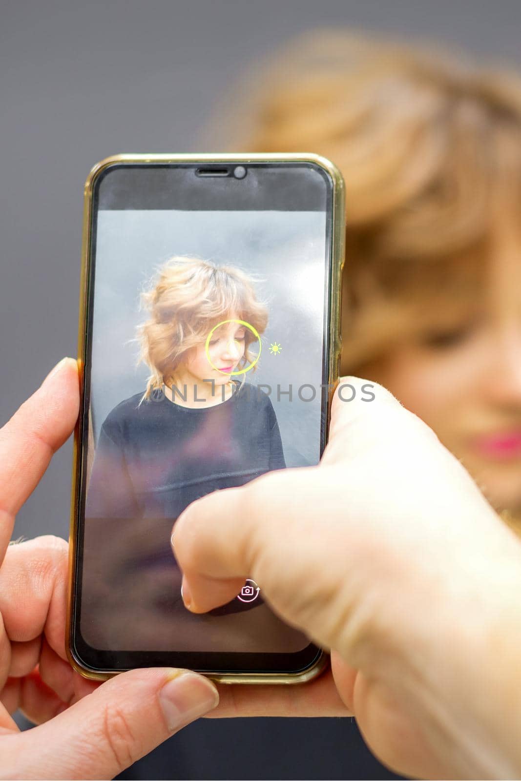 Man hairdresser taking pictures on the smartphone of her client's hairstyle against a gray background