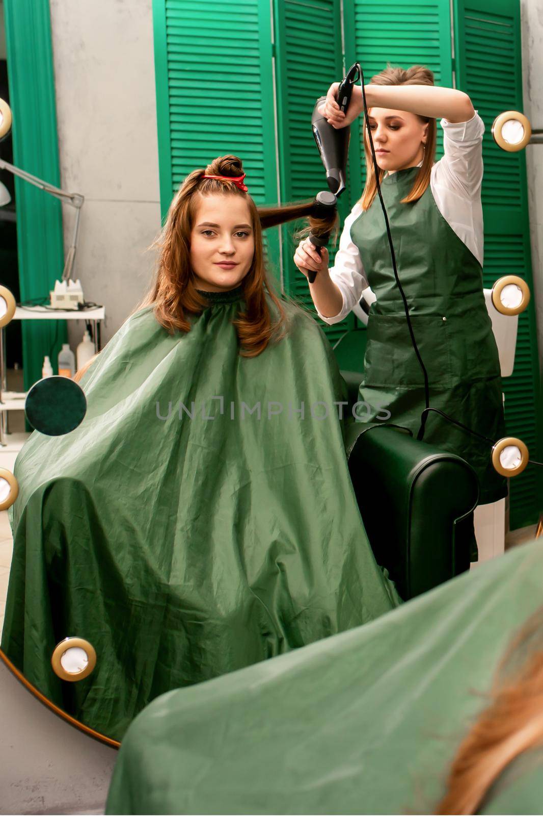 The hairdresser is drying long brown hair with a hairdryer and round brush in a beauty salon