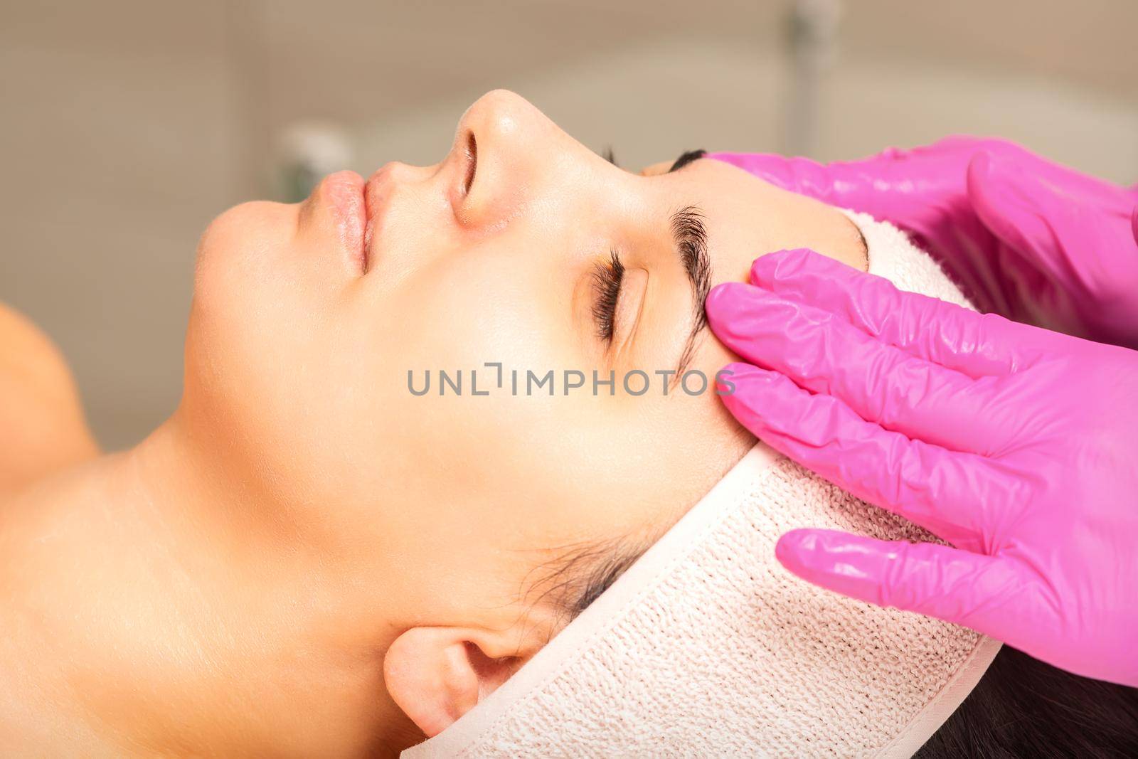 Cosmetologist with gloved hands applies a moisturizing mask with peeling cream on the female face. Facial cosmetology treatment. Procedures for facial care