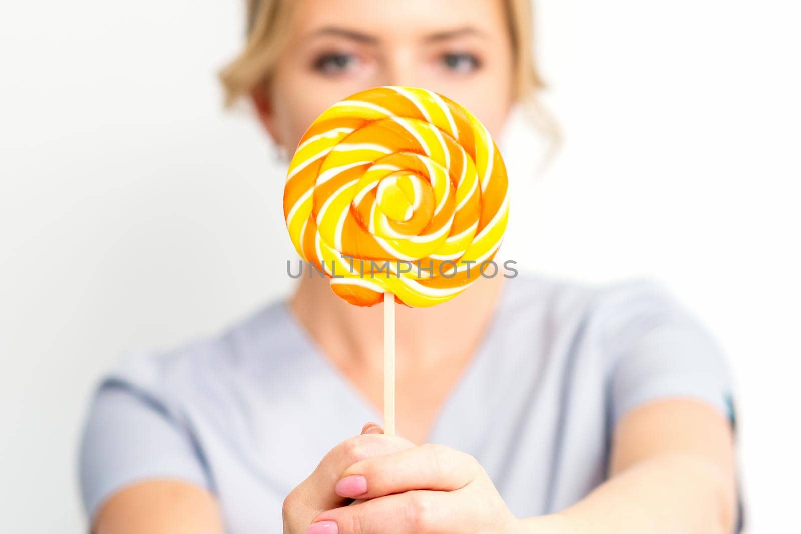 Waxing, depilation concept. The beautician is wearing a medical coat holding a sugar lollipop on white background