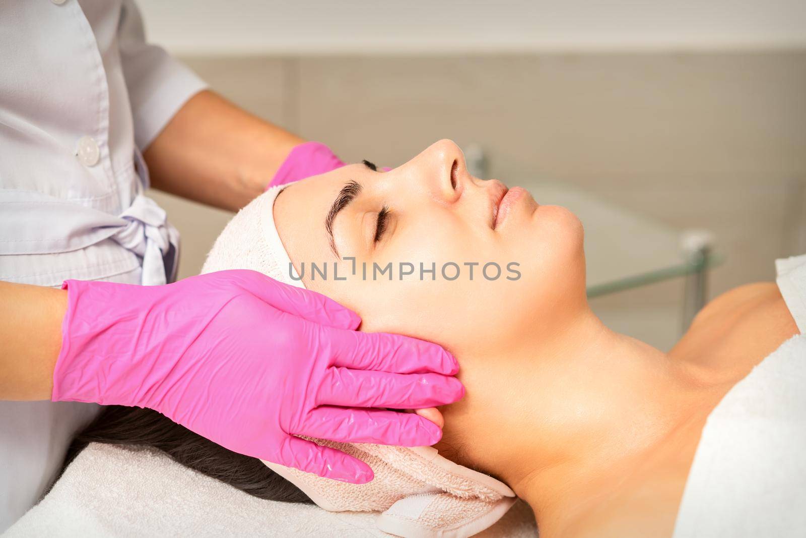 Cosmetologist with gloved hands applies a moisturizing mask with peeling cream on the female face. Facial cosmetology treatment. Procedures for facial care