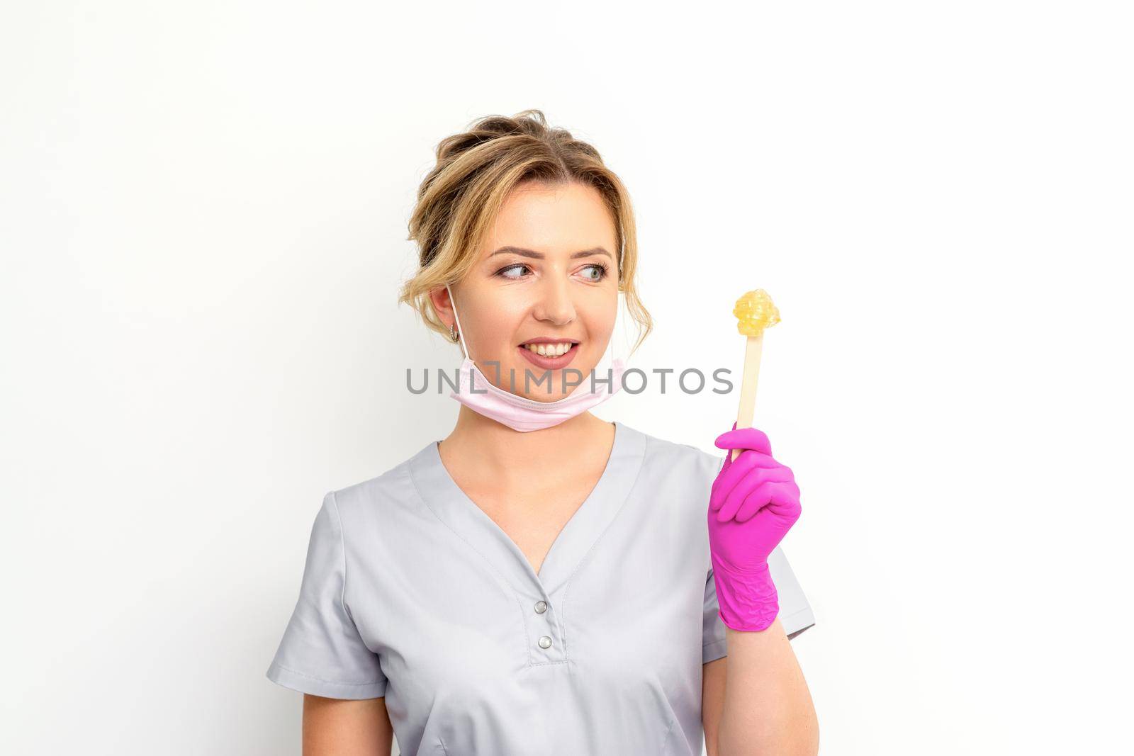 The master of sugar hair removal holds liquid yellow sugar paste, wax for depilation on a wooden stick on a white background