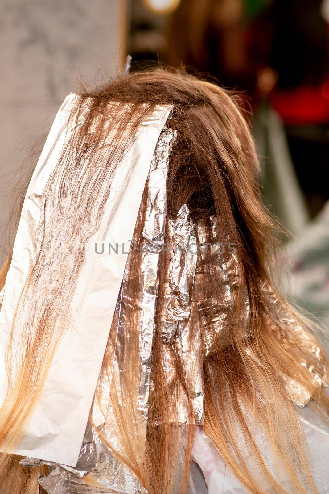 Beautiful young caucasian woman with foil in her hair while dyeing her hair sitting in a beauty salon. by okskukuruza