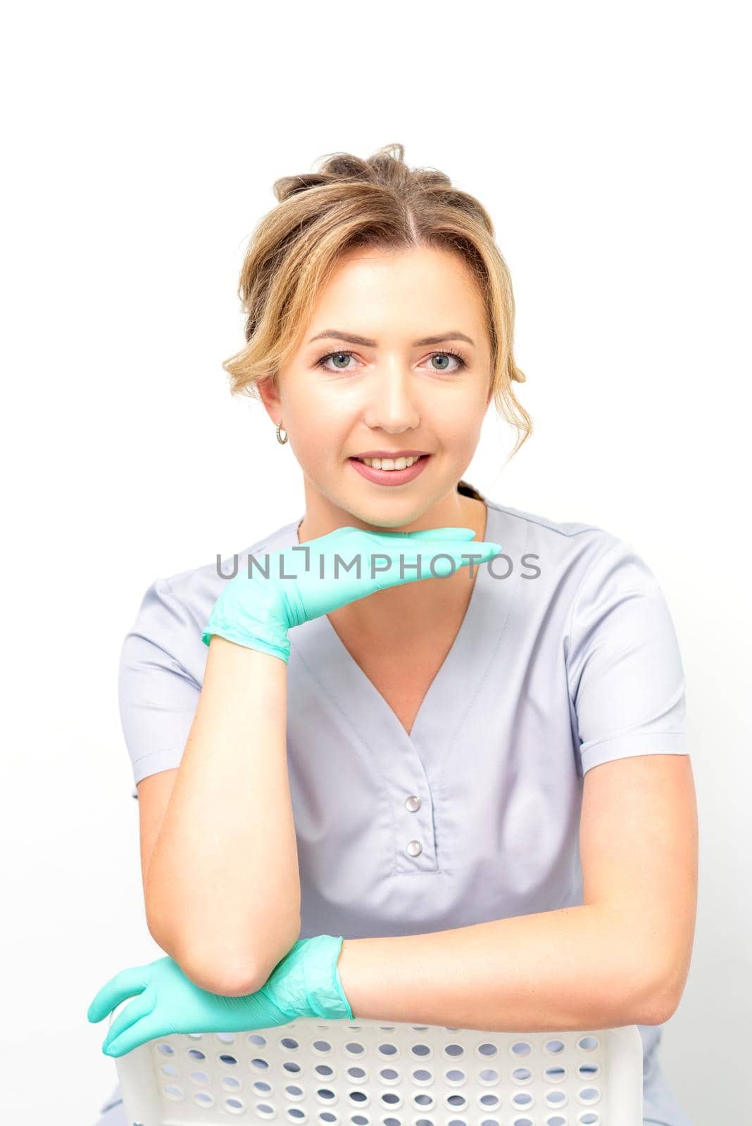 Close-up portrait of young smiling female caucasian healthcare worker sitting and staring at the camera wearing gloves on white background. by okskukuruza