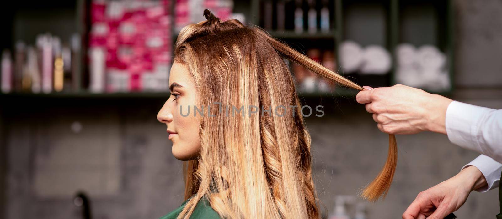 Professional hair care. Beautiful young caucasian blonde woman with long hair receiving hairstyling in a beauty salon. by okskukuruza