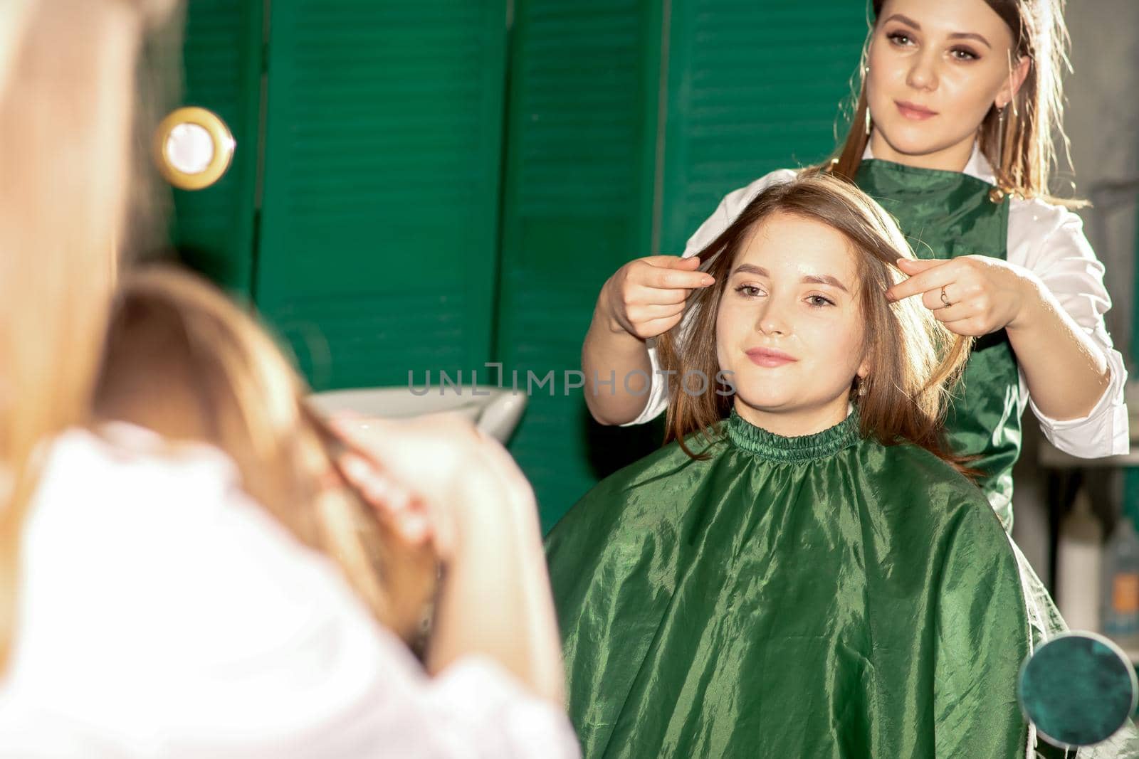 Professional hair care. Beautiful young caucasian brunette woman with long hair receiving hairstyling in a beauty salon. by okskukuruza