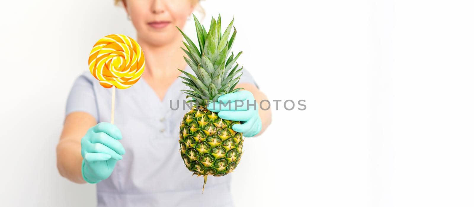 Young caucasian female doctor nutritionist holding fresh pineapple with lollipop over white background