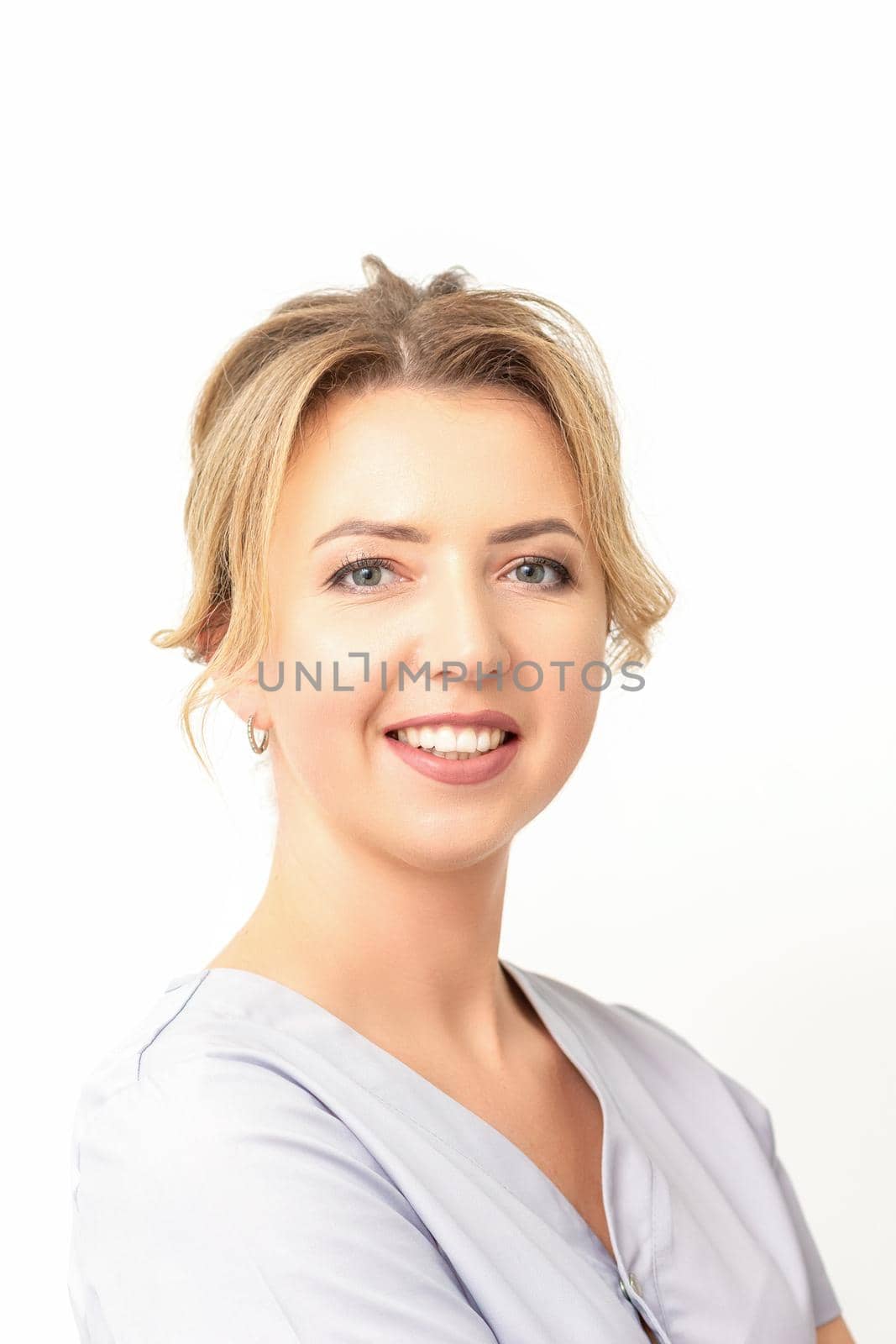 Close-up portrait of young smiling female caucasian healthcare worker standing staring at the camera on white background