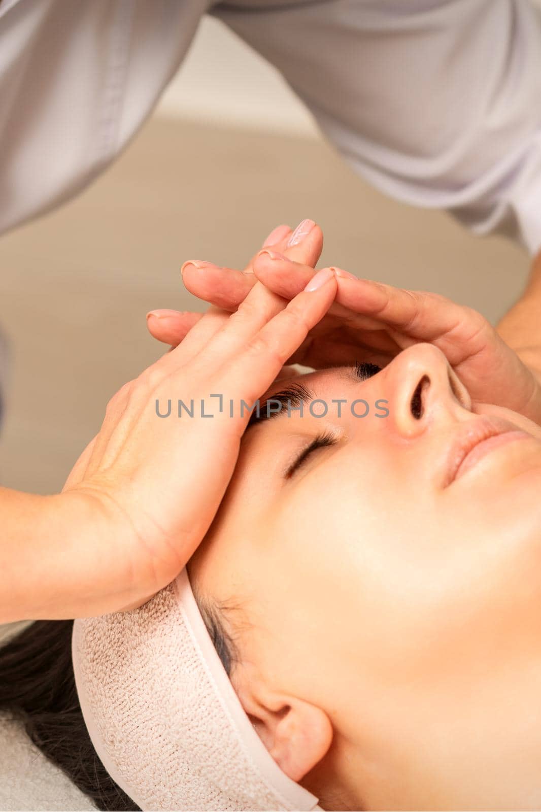 Facial massage. Young caucasian woman with closed eyes getting a massage on her forehead in a beauty salon. by okskukuruza